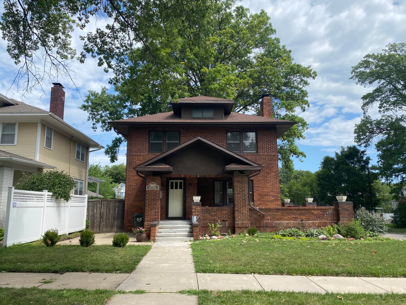 A two-storey brick American Foursquare house in Lincoln with a covered front porch and mature trees.