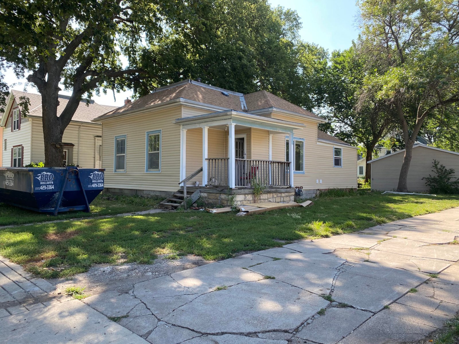 An older yellow Lincoln bungalow with a roll-off dumpster in the driveway during a cleanout.